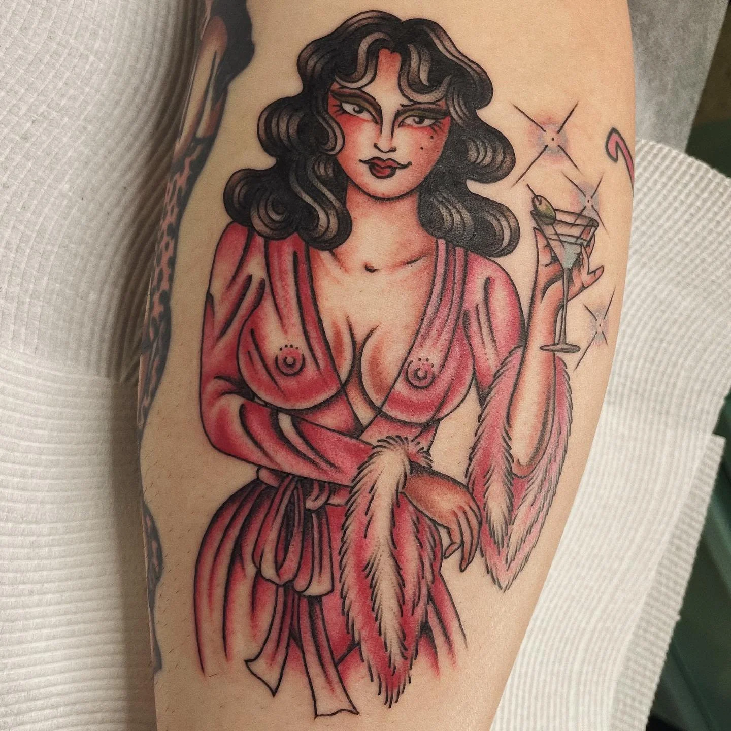 Tattoo of a woman with dark wavy hair, red dress, and a feather in hand, holding a cocktail glass with a lemon garnish.