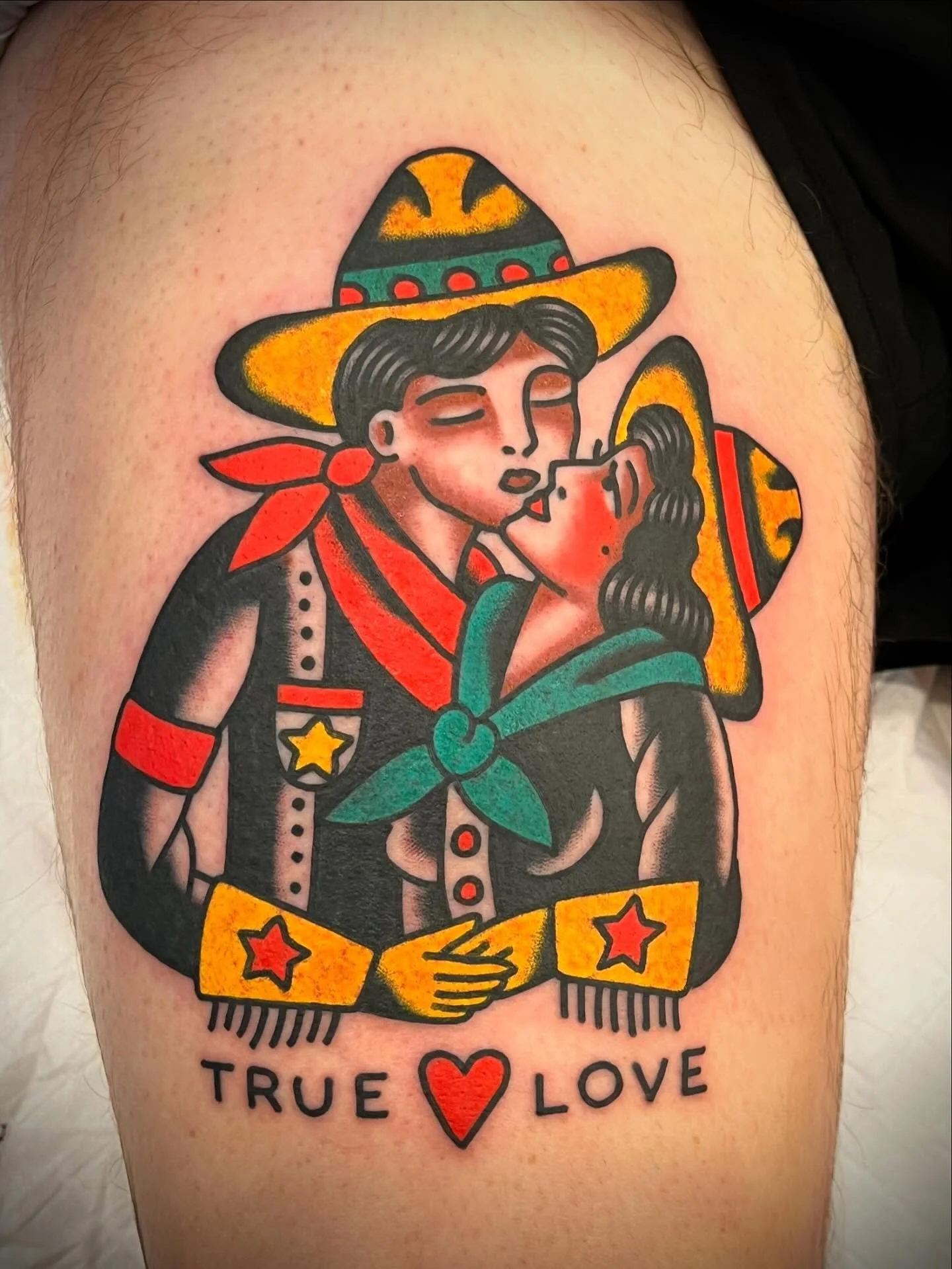 A colorful tattoo of a couple dressed in traditional Mexican attire sharing a kiss, with the words "True Love" and a red heart below.