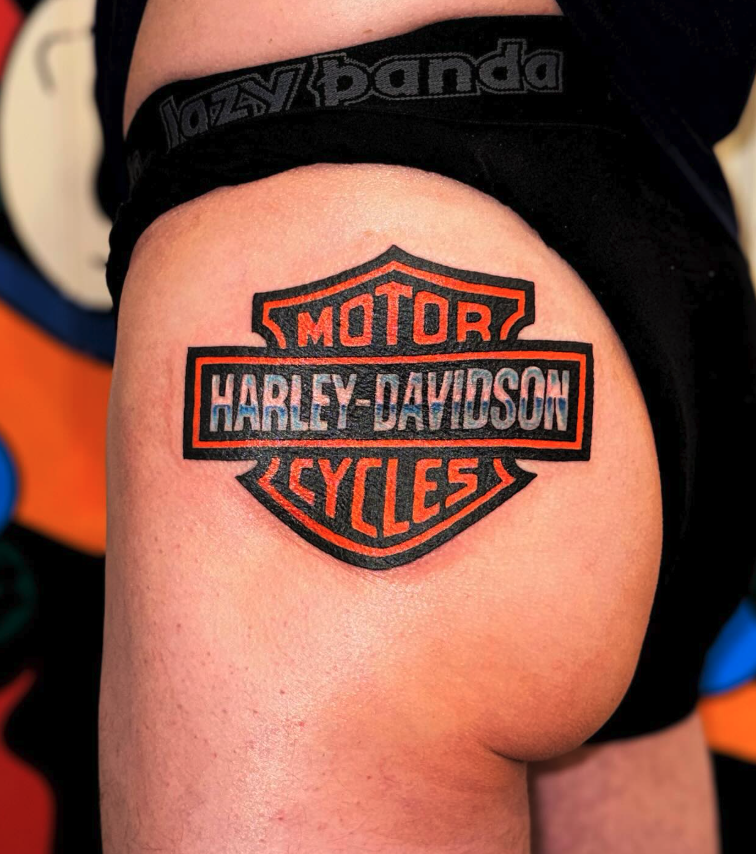 Tattoo of Harley-Davidson logo on person's thigh showing the brand name and iconic shield shape.