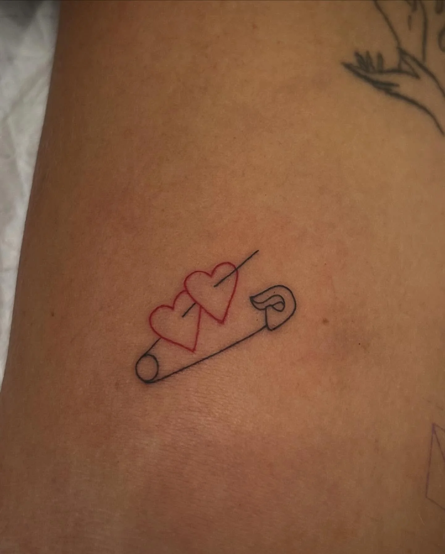 Tattoo of two red hearts with a line running through them, on a skin tone background.