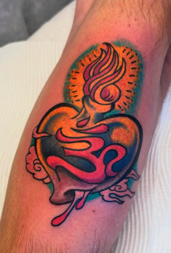 Colorful tattoo on inner forearm featuring a stylized heart with flames, clouds, and vibrant colors.