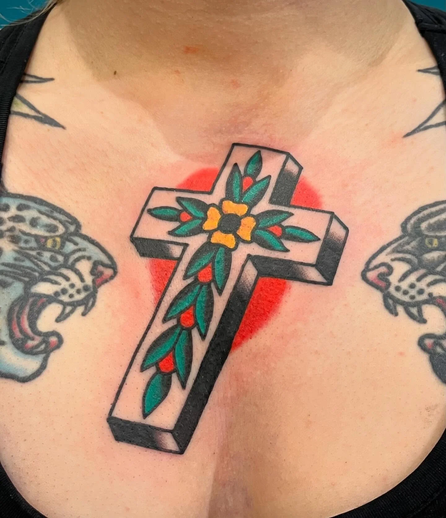 Colorful tattoo of a cross with floral and leaf designs, located on the person's chest