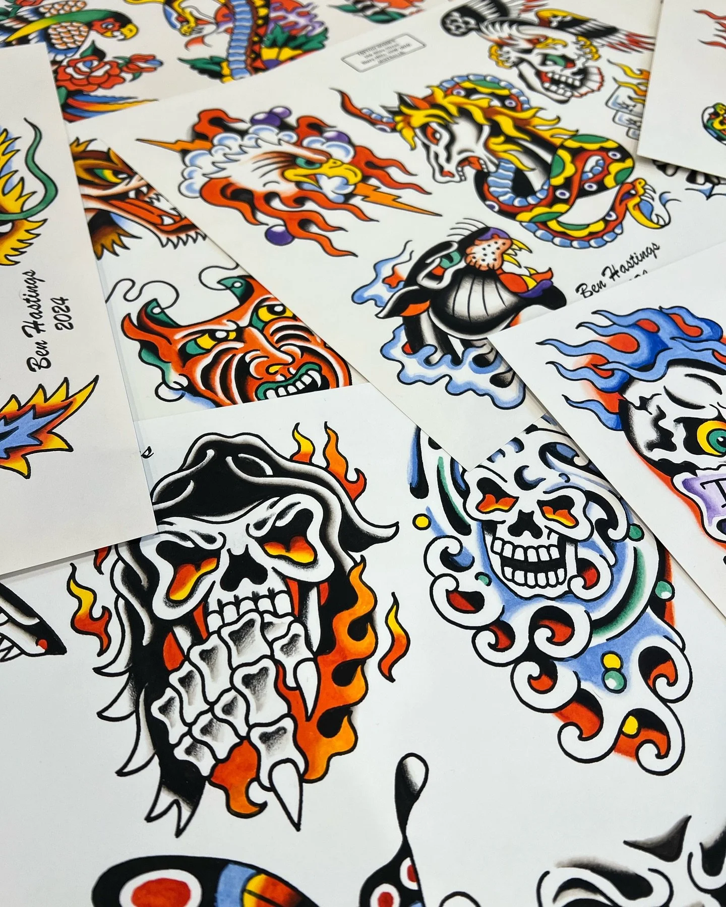 Collection of colorful traditional tattoo-style stickers featuring skulls, dragons, and mythological creatures laid out on a flat surface.