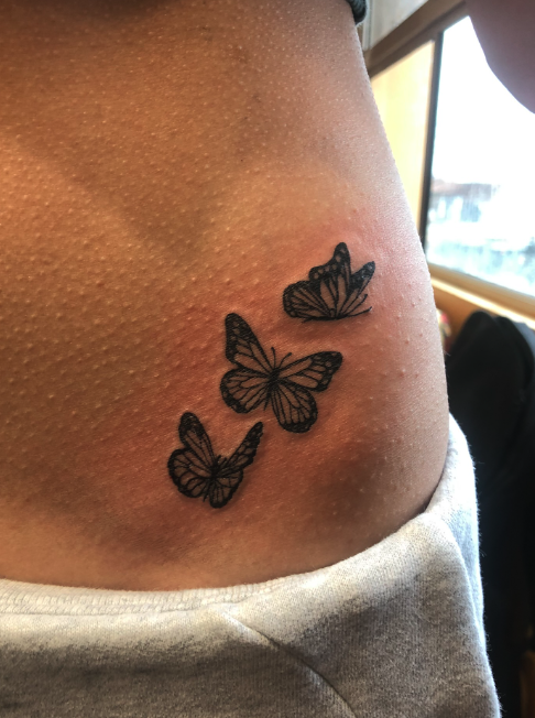 Tattoo of three butterflies on a person's side near the waist.