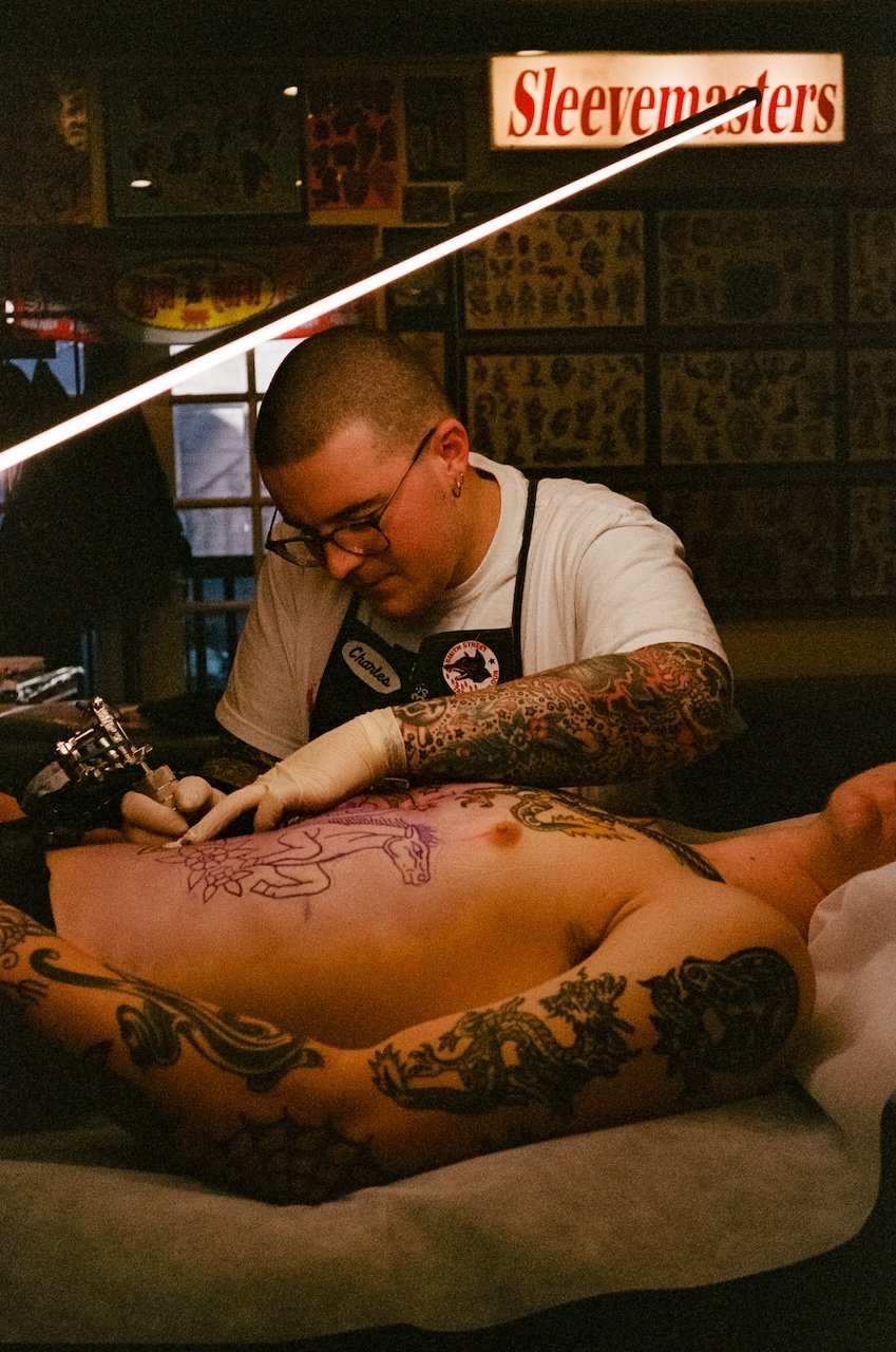 Tattoo artist working on a person's torso in a tattoo shop.