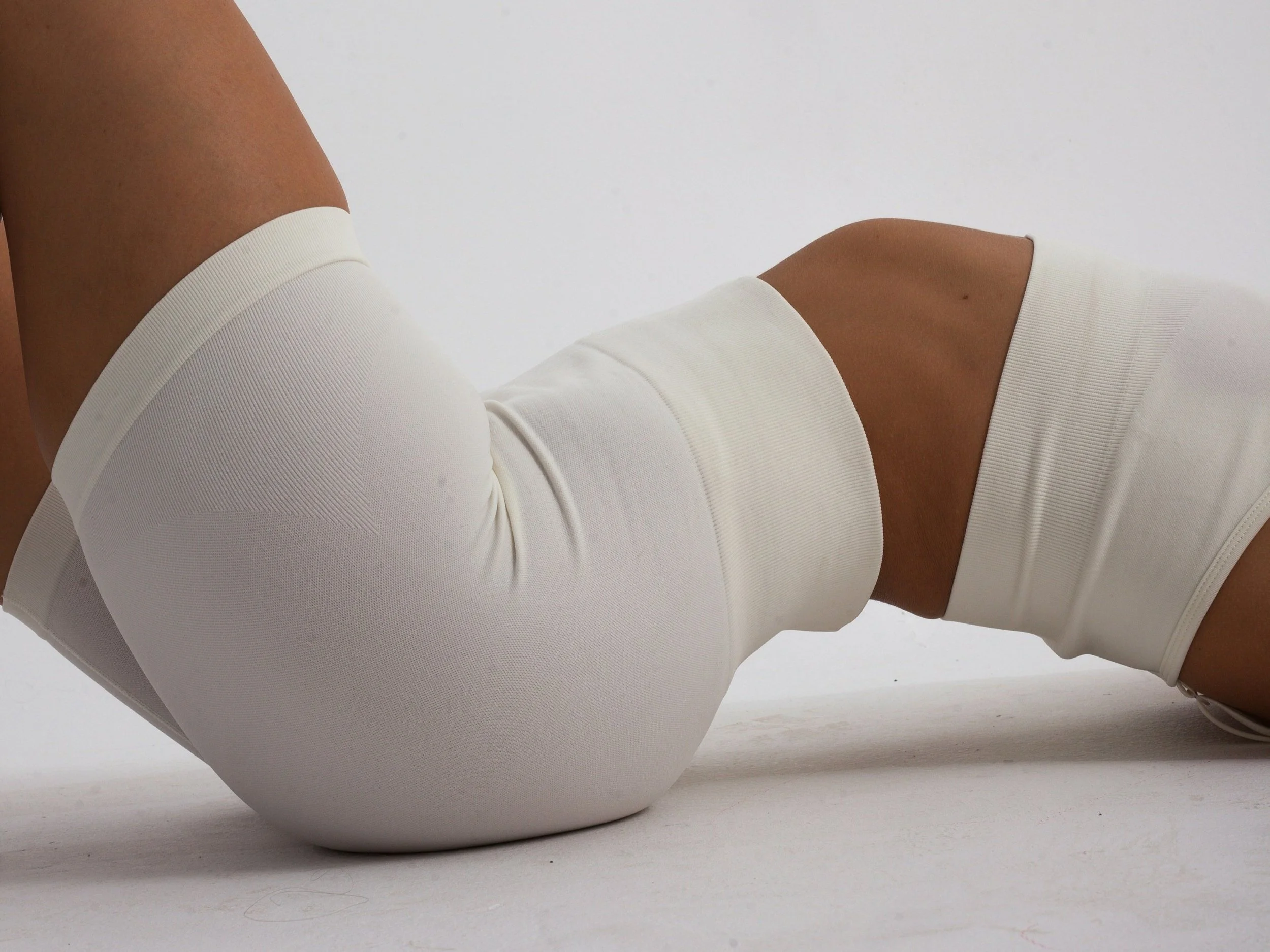 A person lying on their stomach with their legs bent, wearing white sportswear on a plain white background.