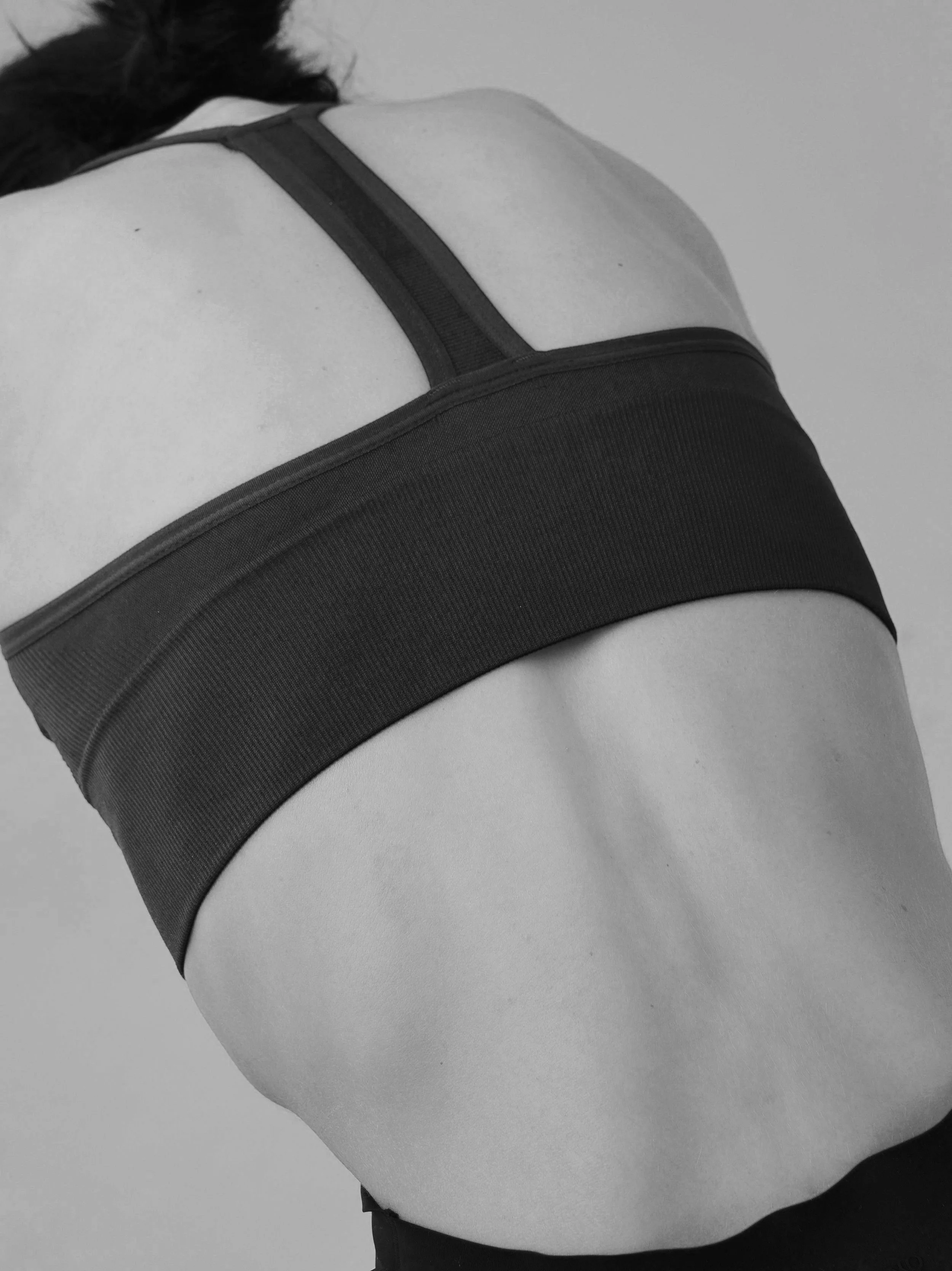 Close-up of a person's back, wearing a black sports bra, with their shoulder and upper back visible.