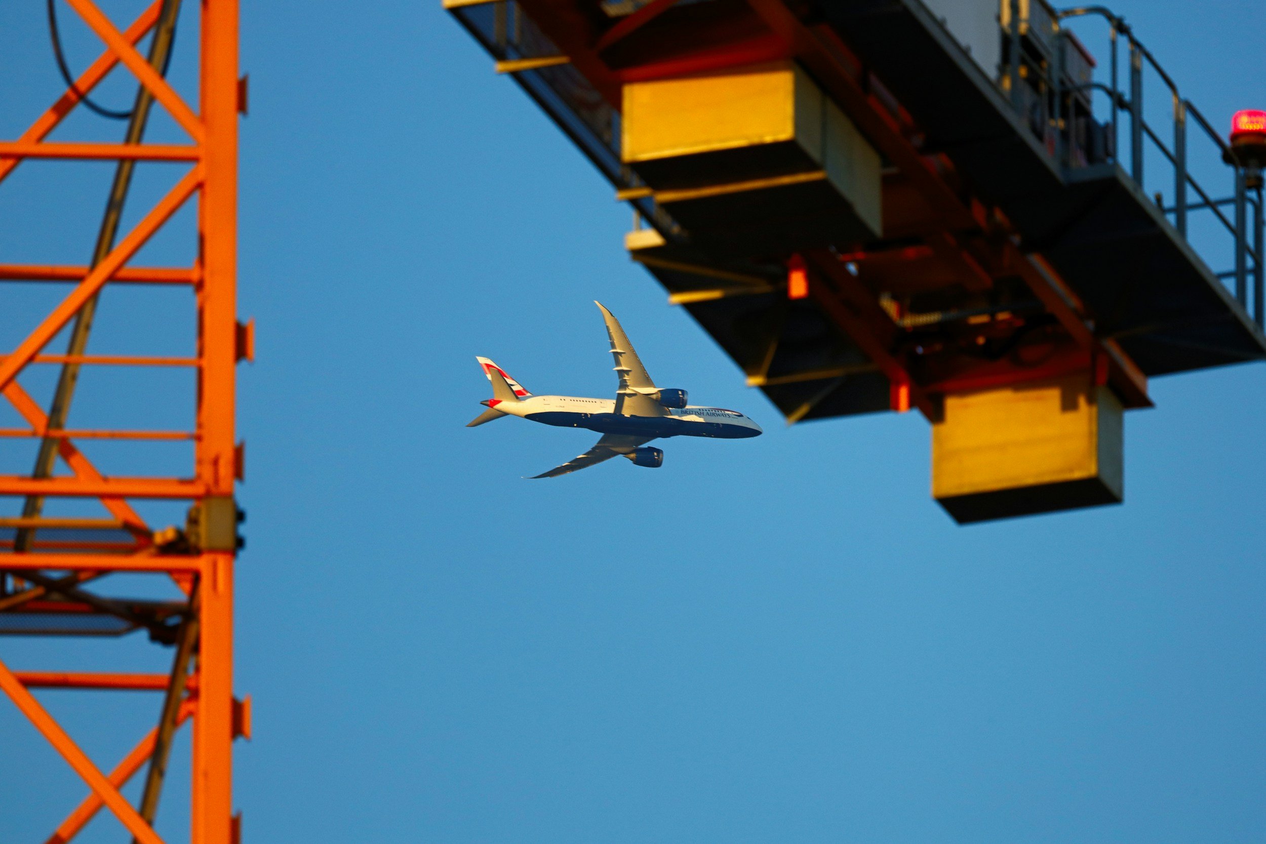 A commercial airplane flying in the sky near a large construction crane.