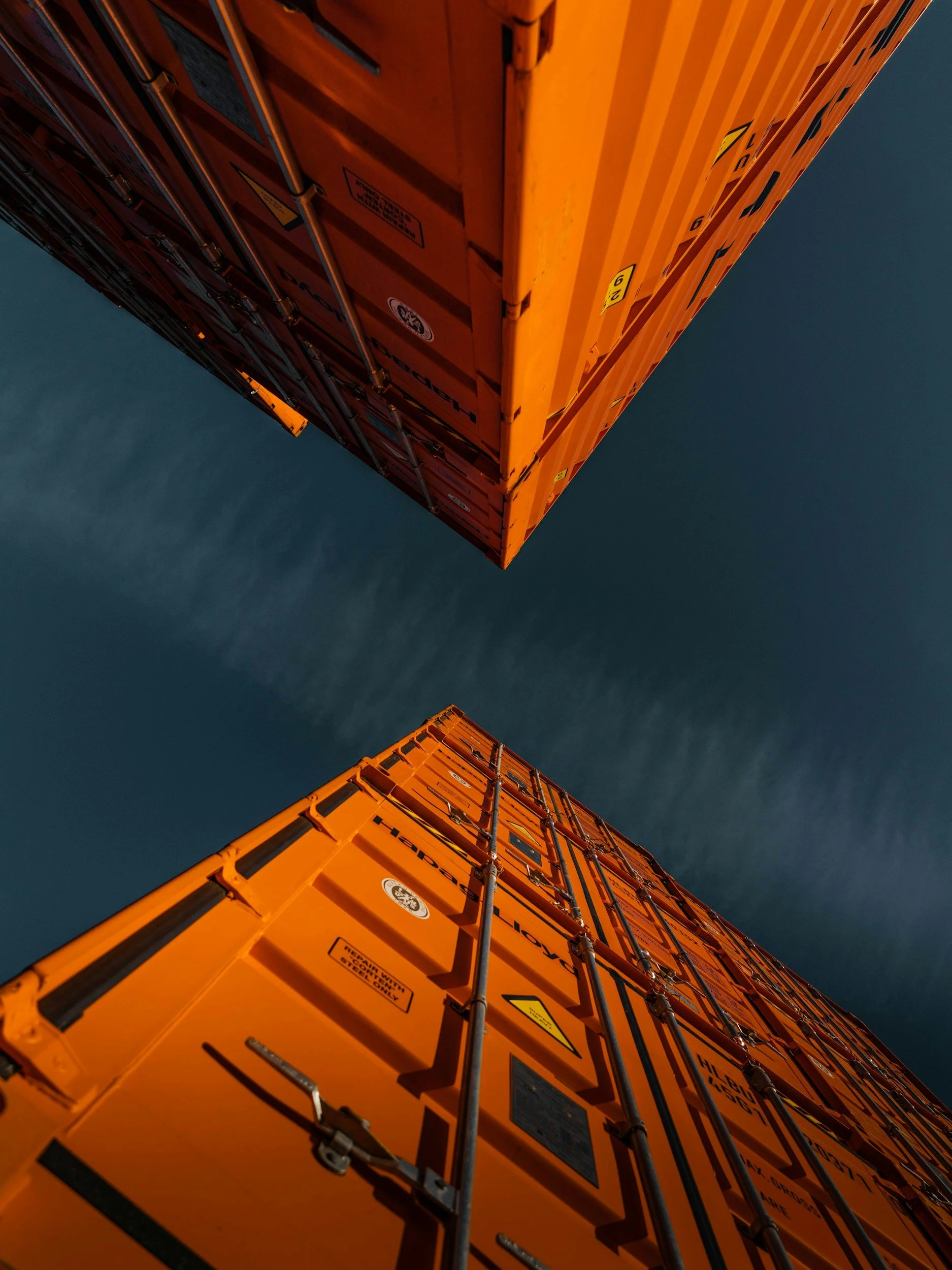 View from below of two stacked orange shipping containers against the sky.