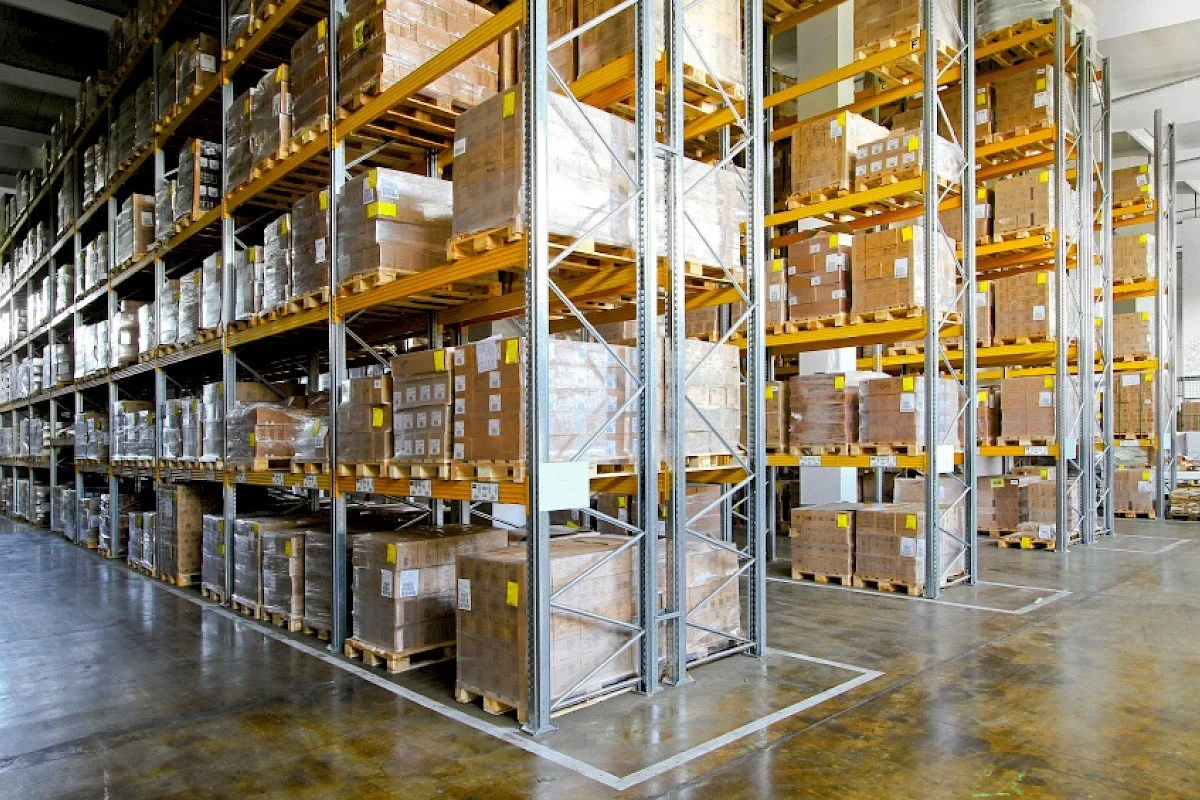 Warehouse with tall metal shelves filled with pallets of boxes and goods, organized for storage.
