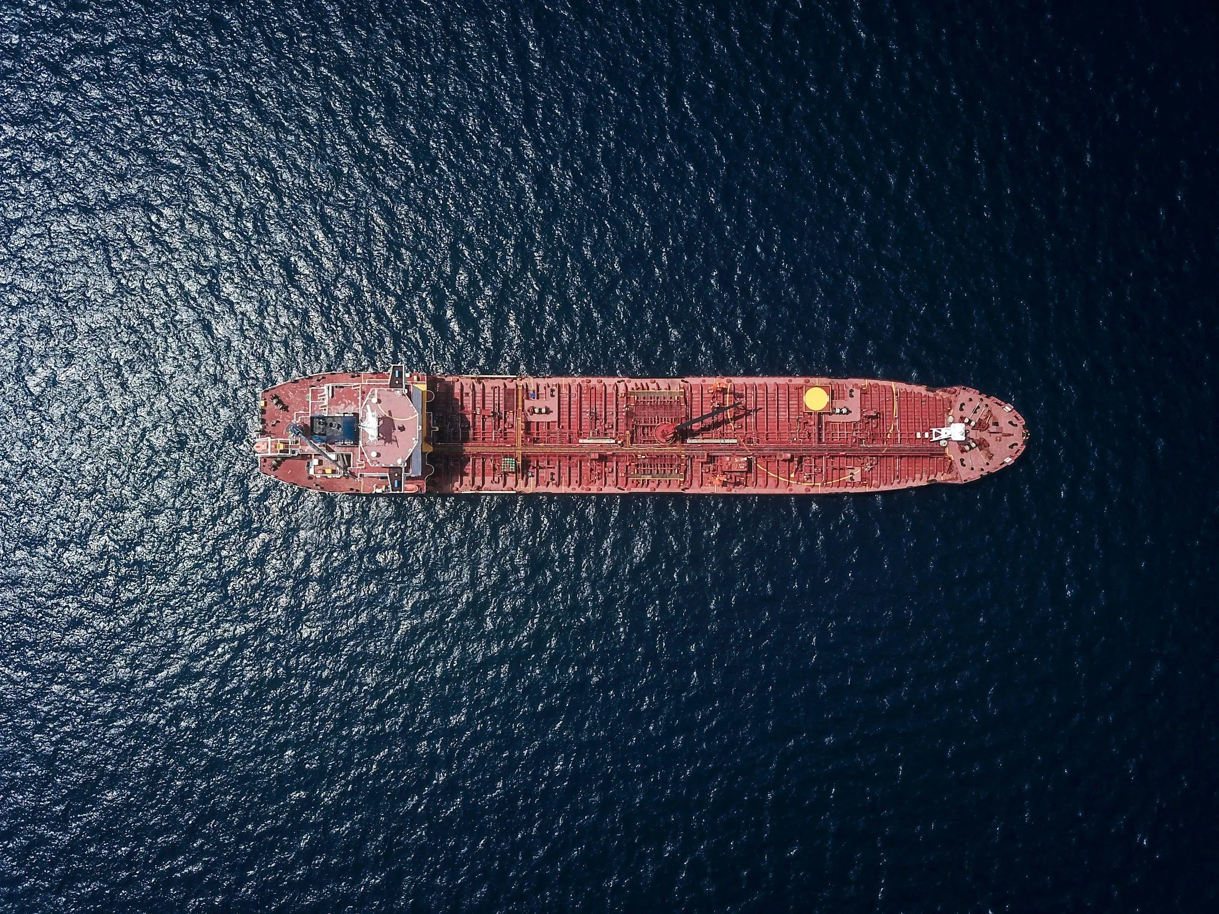 Aerial view of a large red cargo ship sailing in dark blue ocean water.