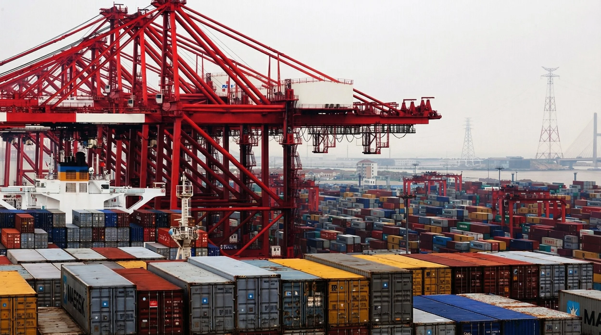 A large shipping port with numerous stacked shipping containers and red cranes for loading and unloading ships.