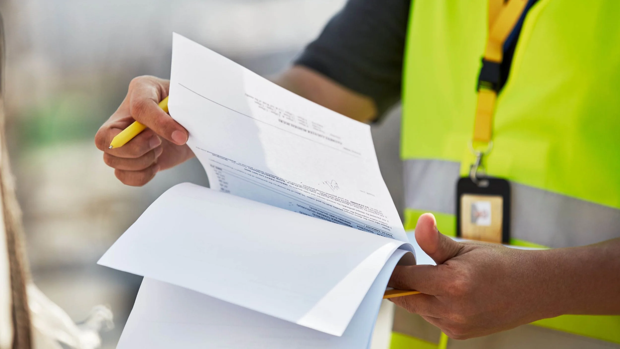 Person holding a stack of papers or documents, wearing a high-visibility safety vest.
