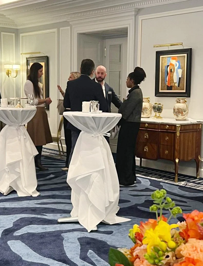 Menschen bei einer Netzwerkveranstaltung in einem eleganten Raum mit Kunstwerken an den Wänden und hohen Decken.