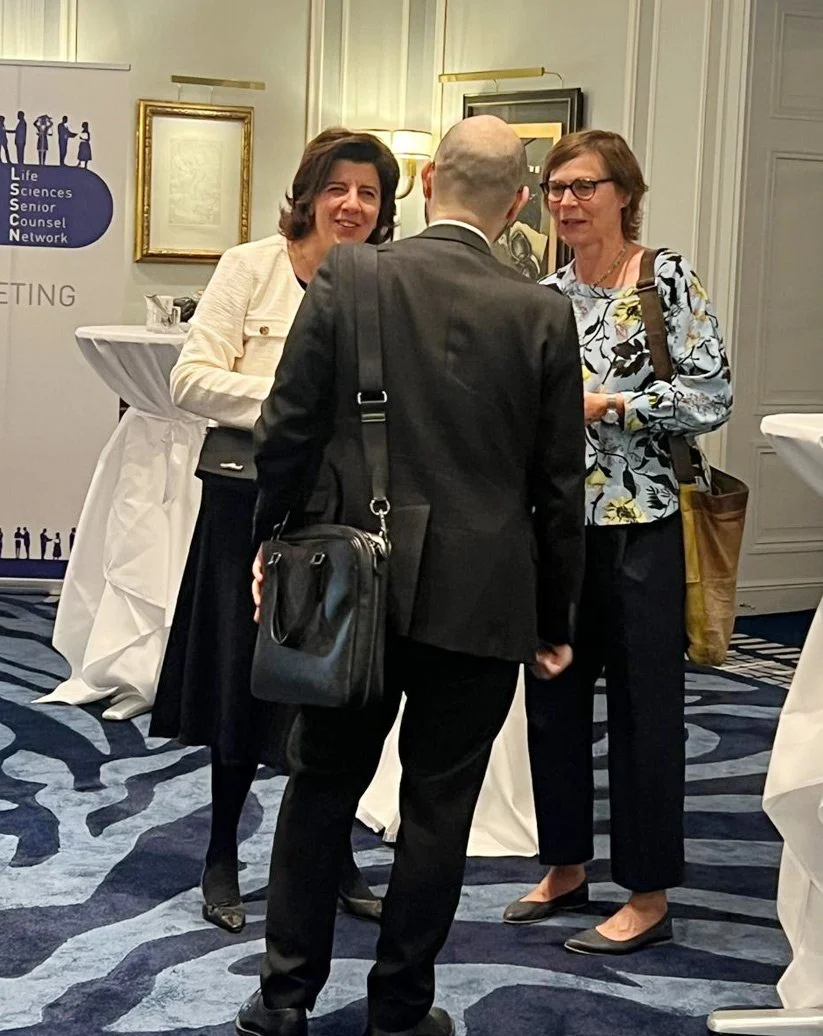 Drei Menschen unterhalten sich auf einer formellen Veranstaltung in einem eleganten Raum mit Tapeten und Kunstwerken an den Wänden.