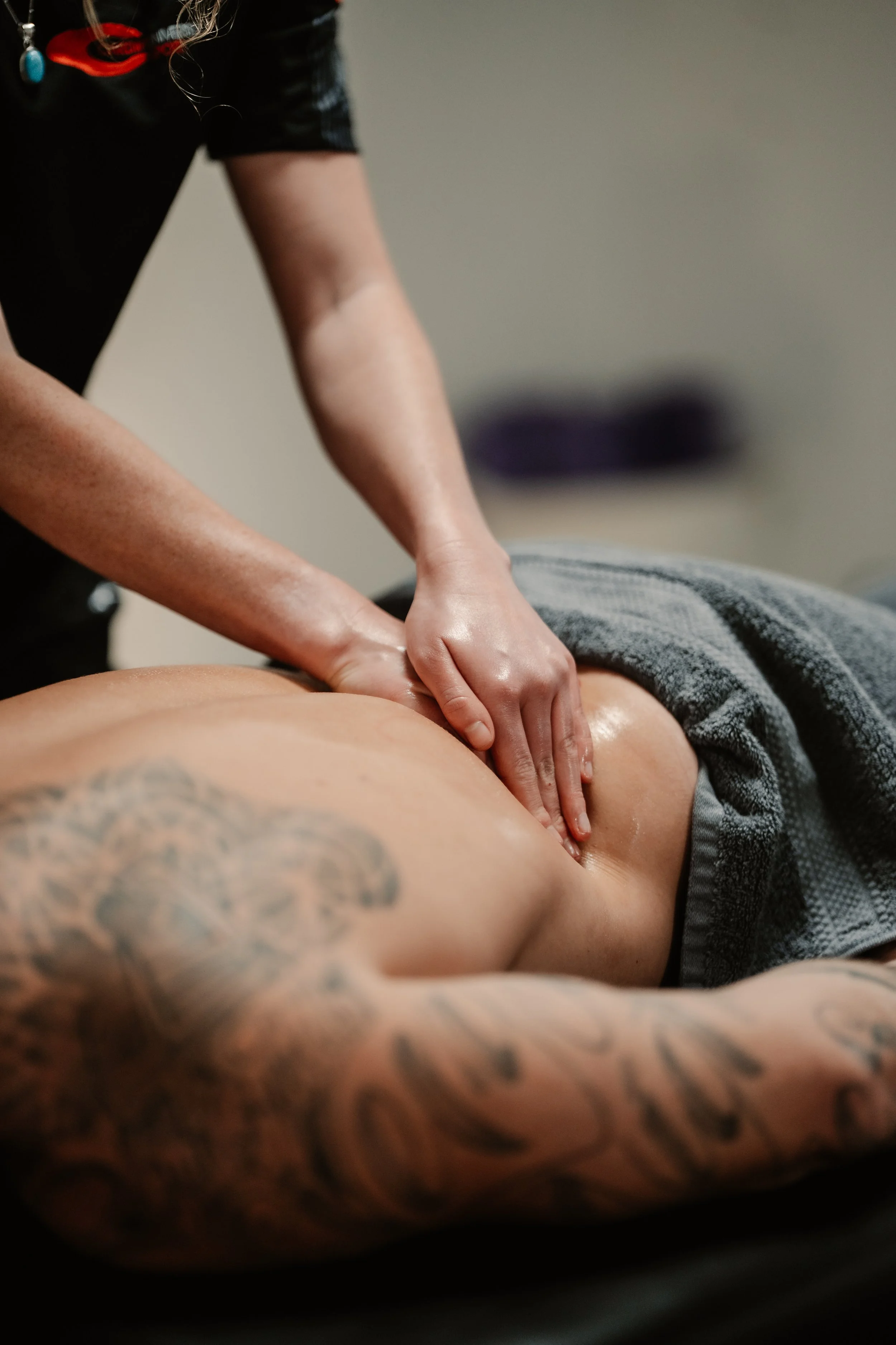 A massage therapist giving a back massage to a person lying face down, with their body covered by a towel, in a spa or massage therapy setting.