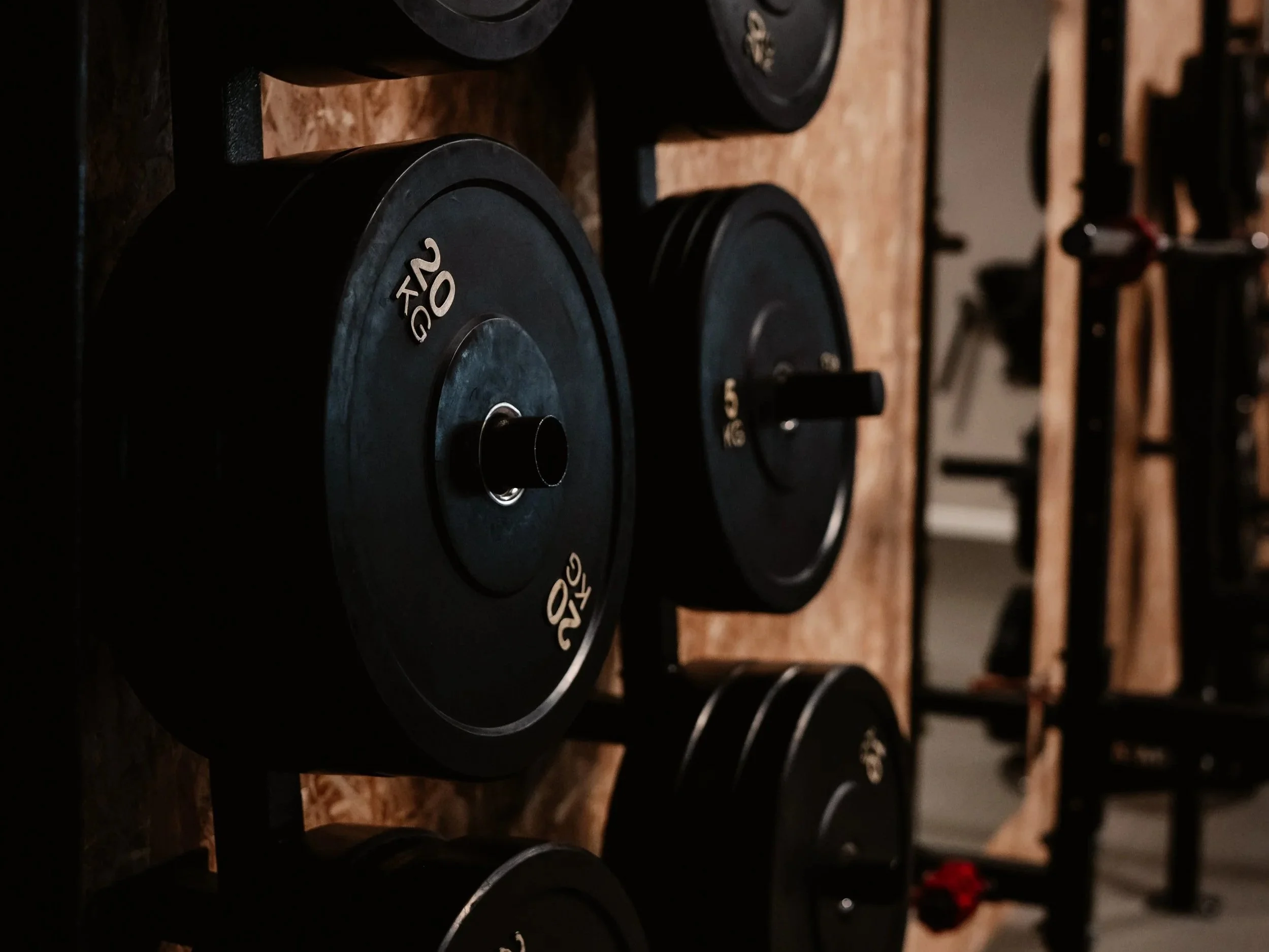 Black weight plates on a rack in a gym, marked with 20 KG and 5 KG, on a wooden surface.