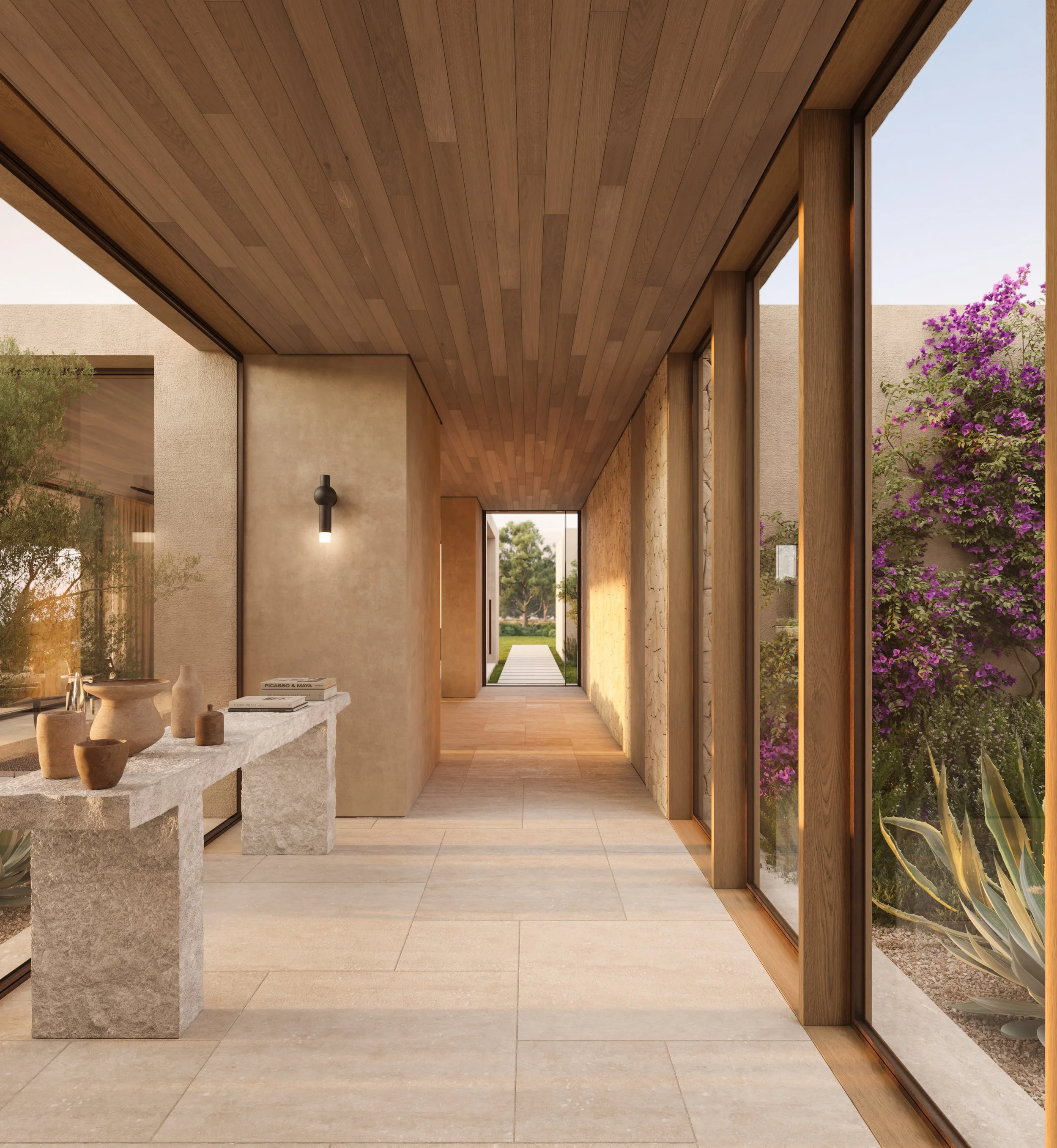 Pasillo luminoso con paredes de piedra, paredes de estuco y ventanales de madera, con plantas y césped en el exterior.