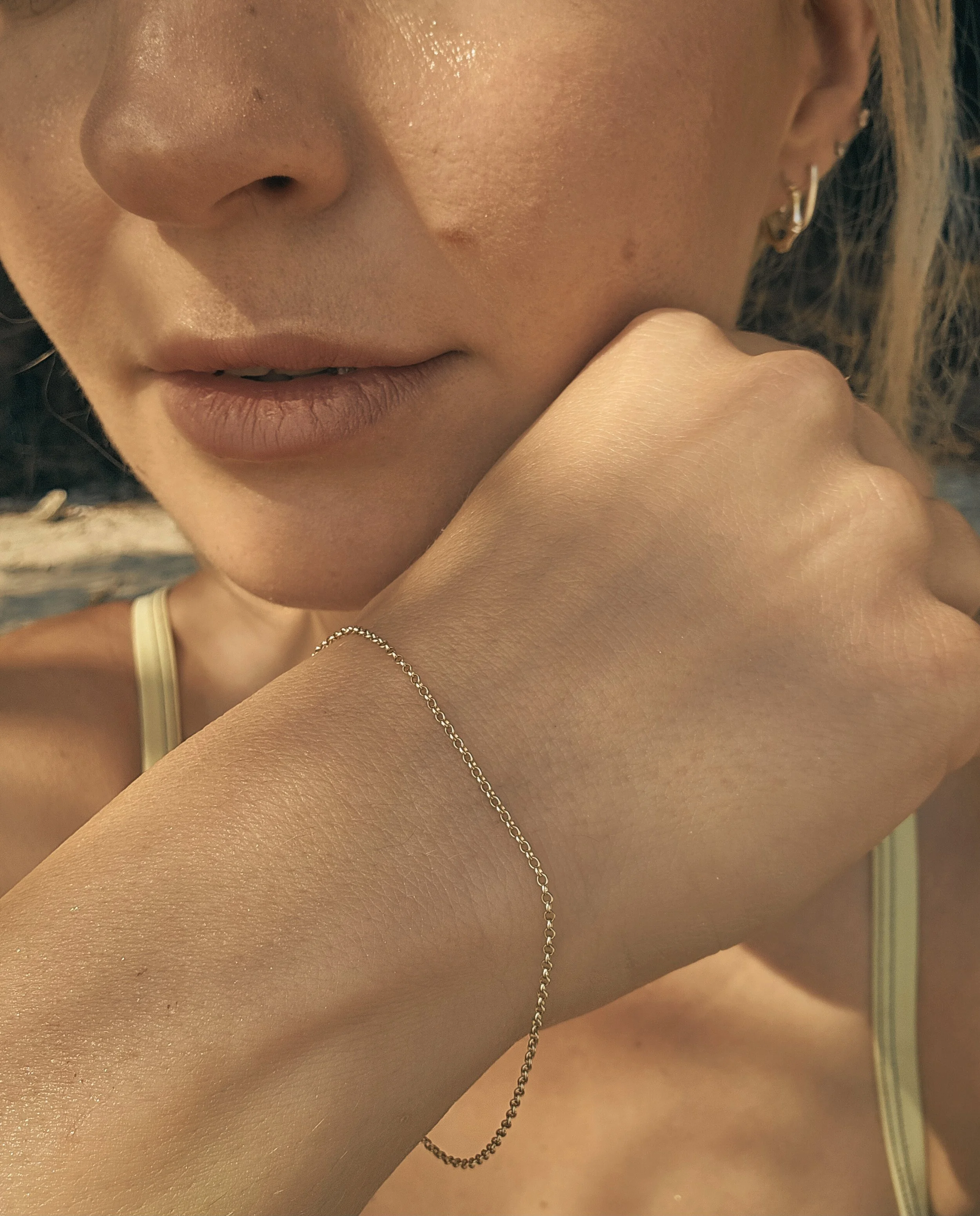A close-up of a woman with a bracelet on her wrist, wearing a yellow ABYSSE swim suit, and resting her chin on her hand.