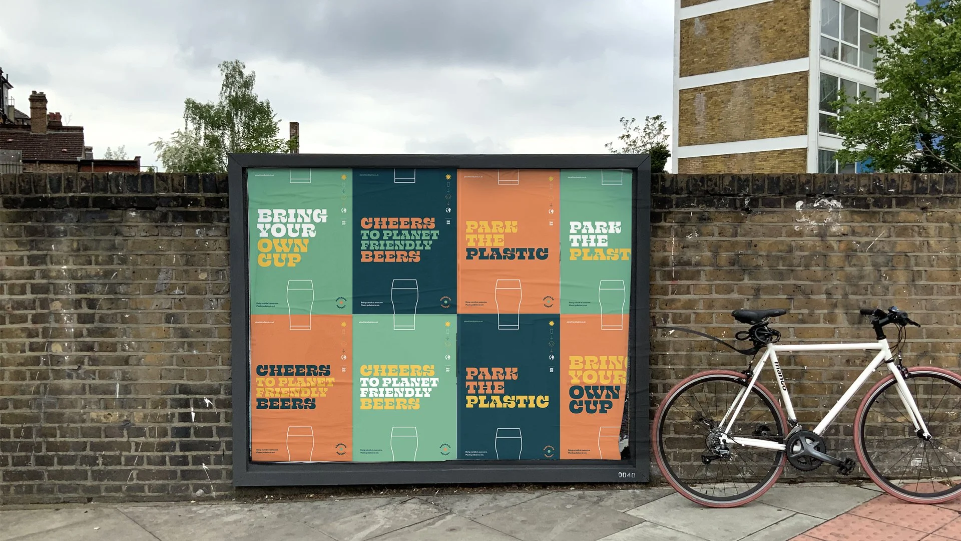 Panneau d'affichage avec des affiches colorées portant des messages liés à l'environnement et à la consommation responsable, placé devant un mur en briques et avec un vélo blanc à côté.