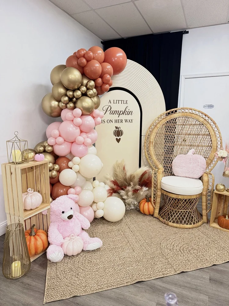 Fall pumpkin baby shower setup with arch backdrop, pink, gold and terracotta balloon garland, peacock chair and pumpkins at Pearl's Event Boutique in Waldorf, Maryland