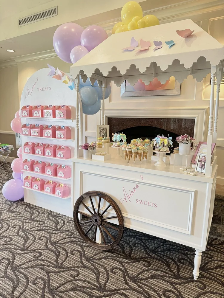 Candy cart rental and shelf backdrop with pink treat boxes, butterflies and pastel balloons at a first birthday at River Creek Club in Leesburg, Virginia