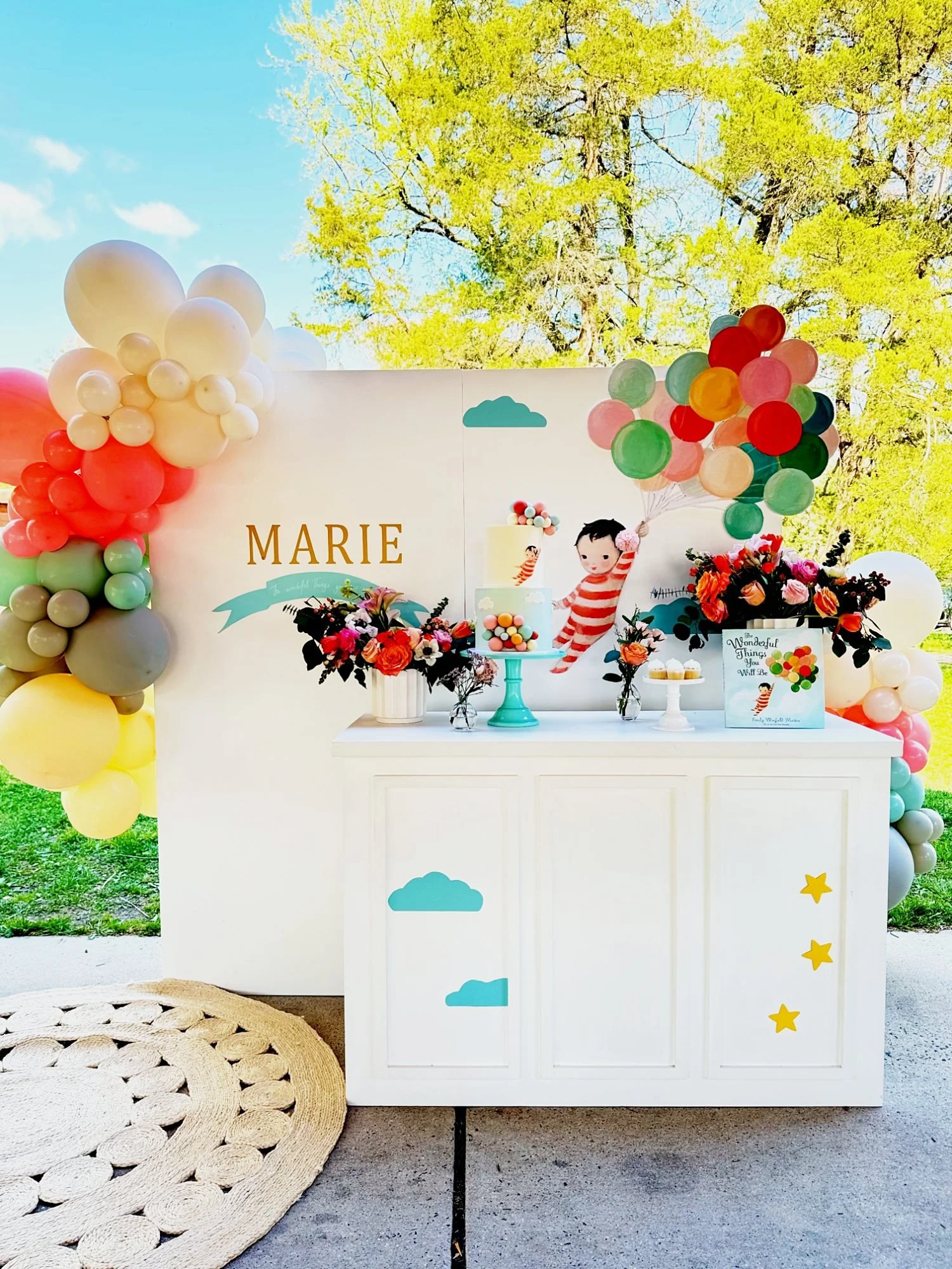 Outdoor park birthday setup with a white backdrop, dessert table, floral arrangements, cake and a pastel balloon garland at Clemyjontri Park in McLean, Virginia