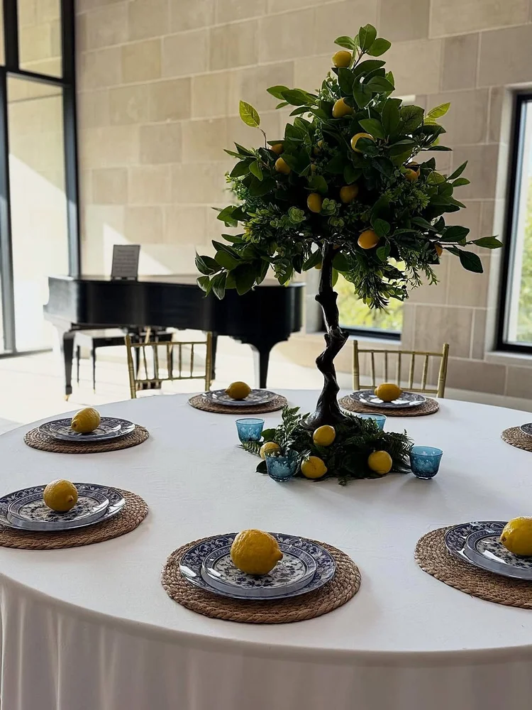 Round table with a lemon tree centerpiece, blue and white china, woven chargers and a lemon at each place setting