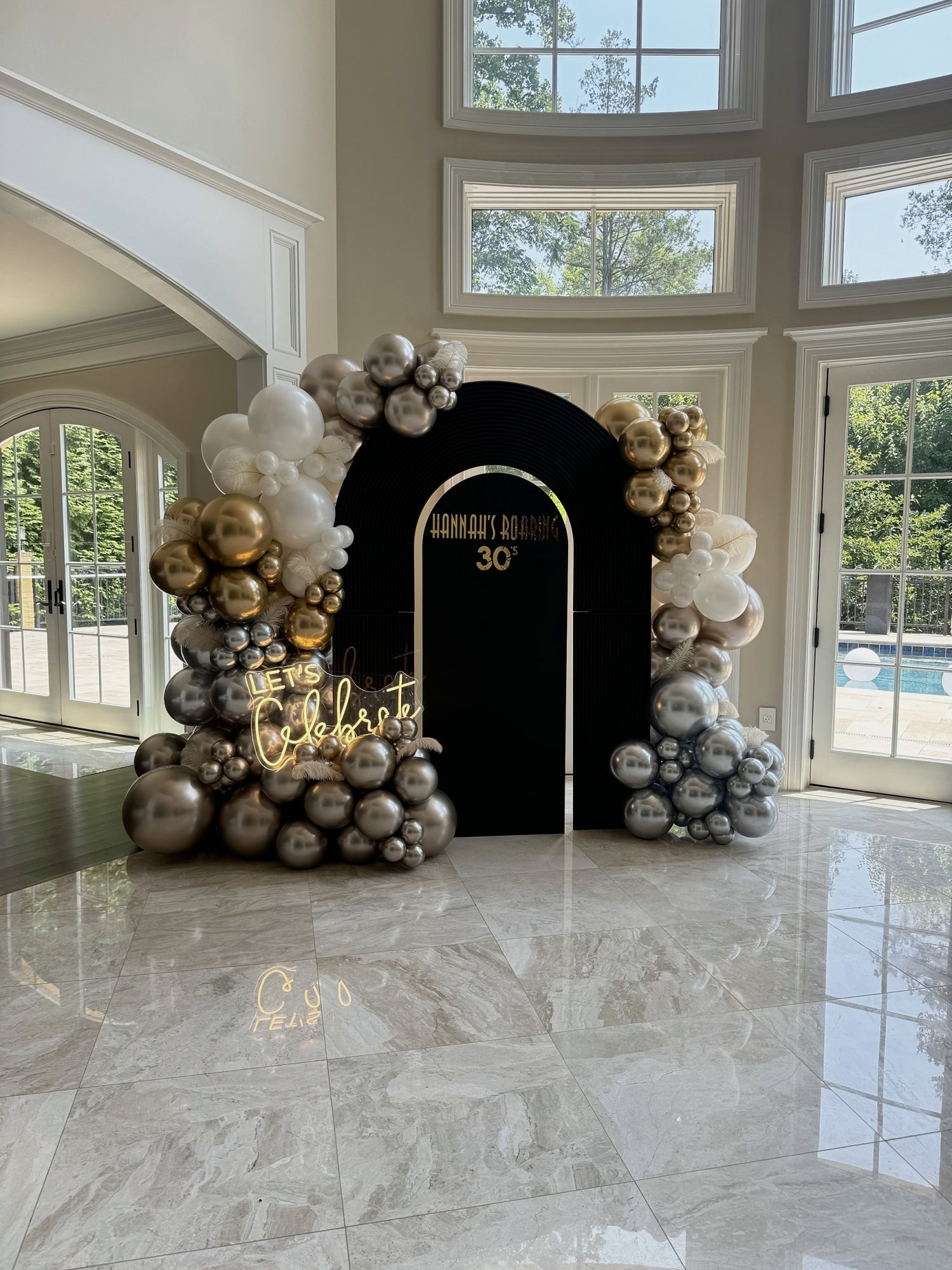 Roaring 20s themed 30th birthday with a black arch backdrop, Let's Celebrate neon sign and gold, silver and white balloon garlands with feathers in a McLean, Virginia home