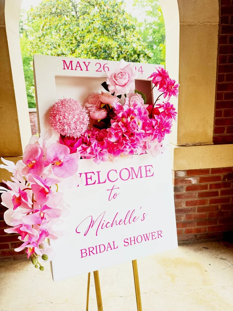 Bridal shower welcome sign on a gold easel with a pink floral arrangement at Sully Station Community Association in Centreville, Virginia