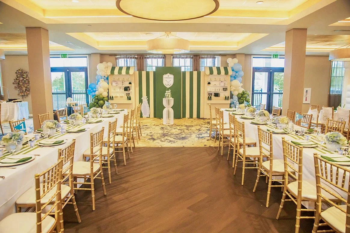 Golf themed hole-in-one first birthday with a green striped backdrop, balloon garlands and banquet tables at Dominion Valley Country Club in Haymarket, VA