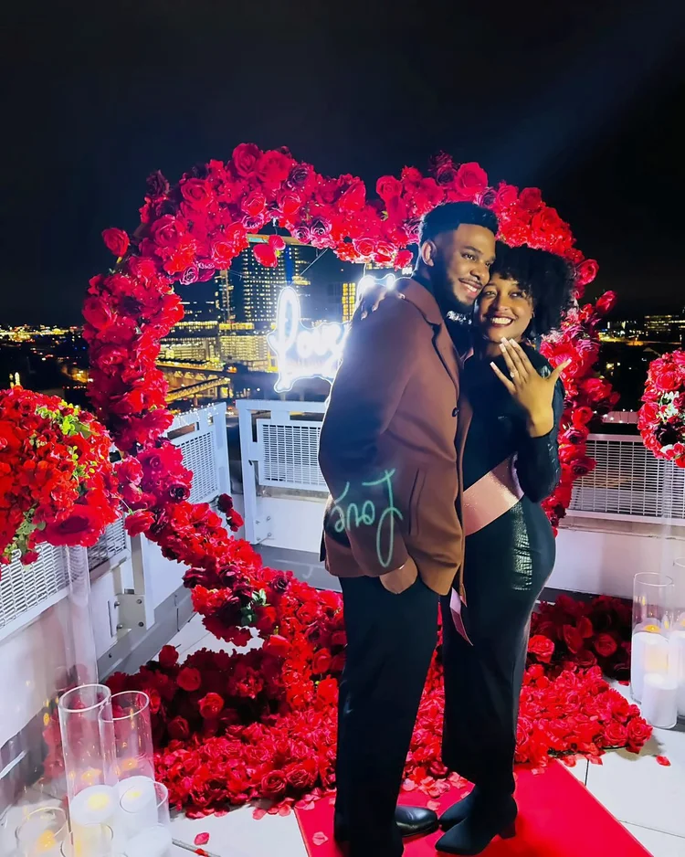 Couple celebrating their engagement in front of a red rose heart arch with a neon sign at Mia Penthouse, the rooftop space at The Watermark Hotel in Tysons Corner, McLean, Virginia