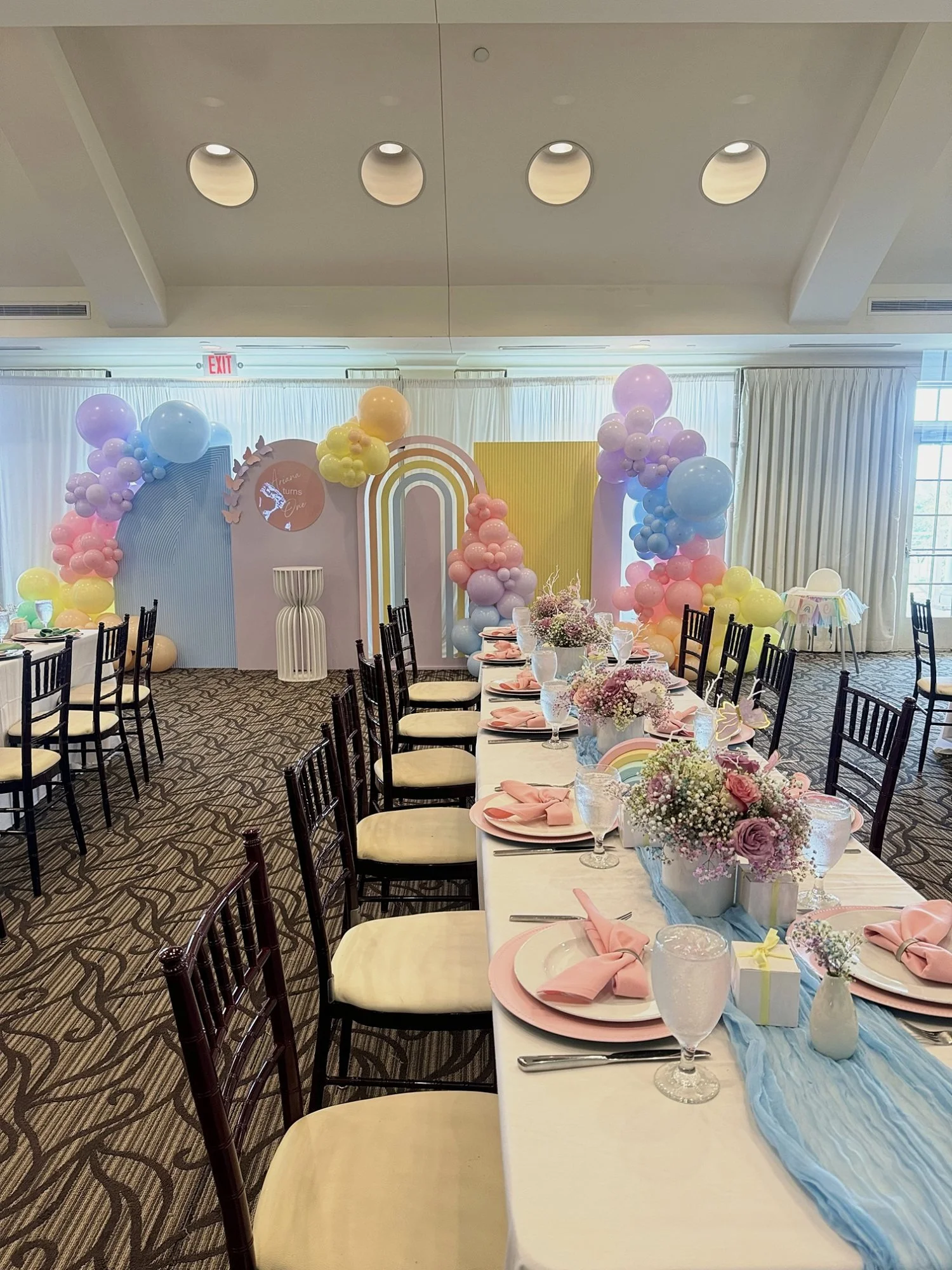 Pastel rainbow first birthday setup with arch backdrops, balloon garlands and a styled guest table at River Creek Club in Leesburg, Virginia