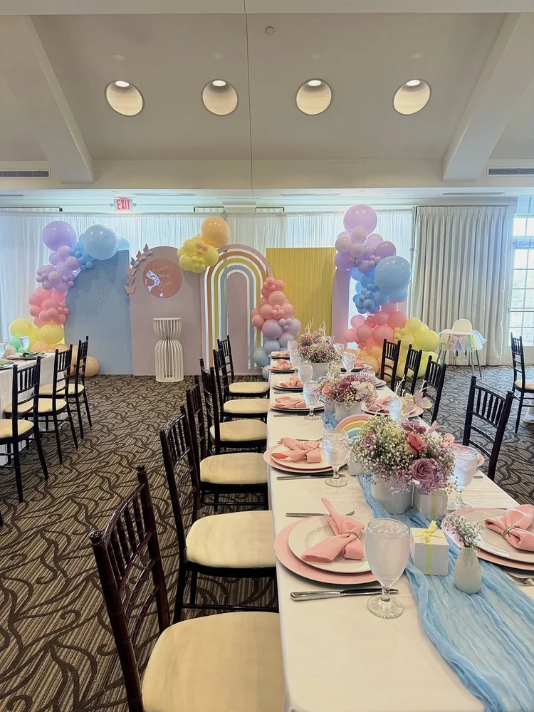 Pastel rainbow first birthday setup with arch backdrops, balloon garlands and a styled guest table at River Creek Club in Leesburg, Virginia