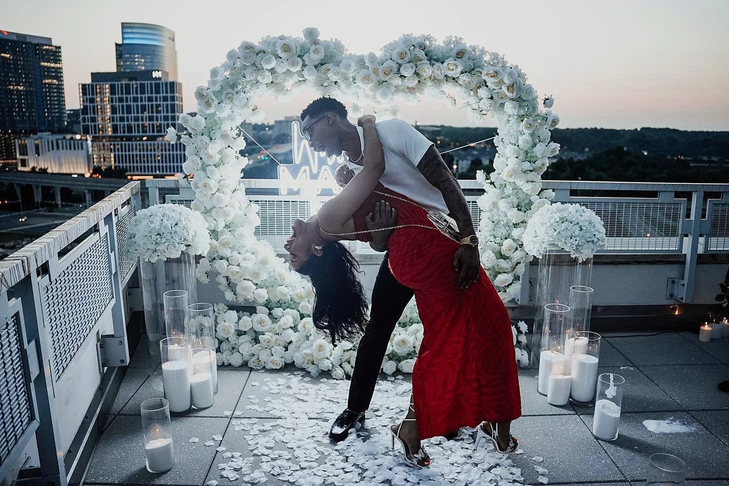 Couple celebrating after a proposal in front of a white rose heart arch with candles and petals at Mia Penthouse, the rooftop space at The Watermark Hotel in Tysons Corner, McLean, Virginia