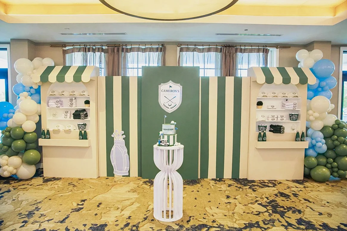 Golf first birthday shop-front style backdrop with green stripes, cake stand and balloon garlands at Dominion Valley Country Club in Haymarket, VA