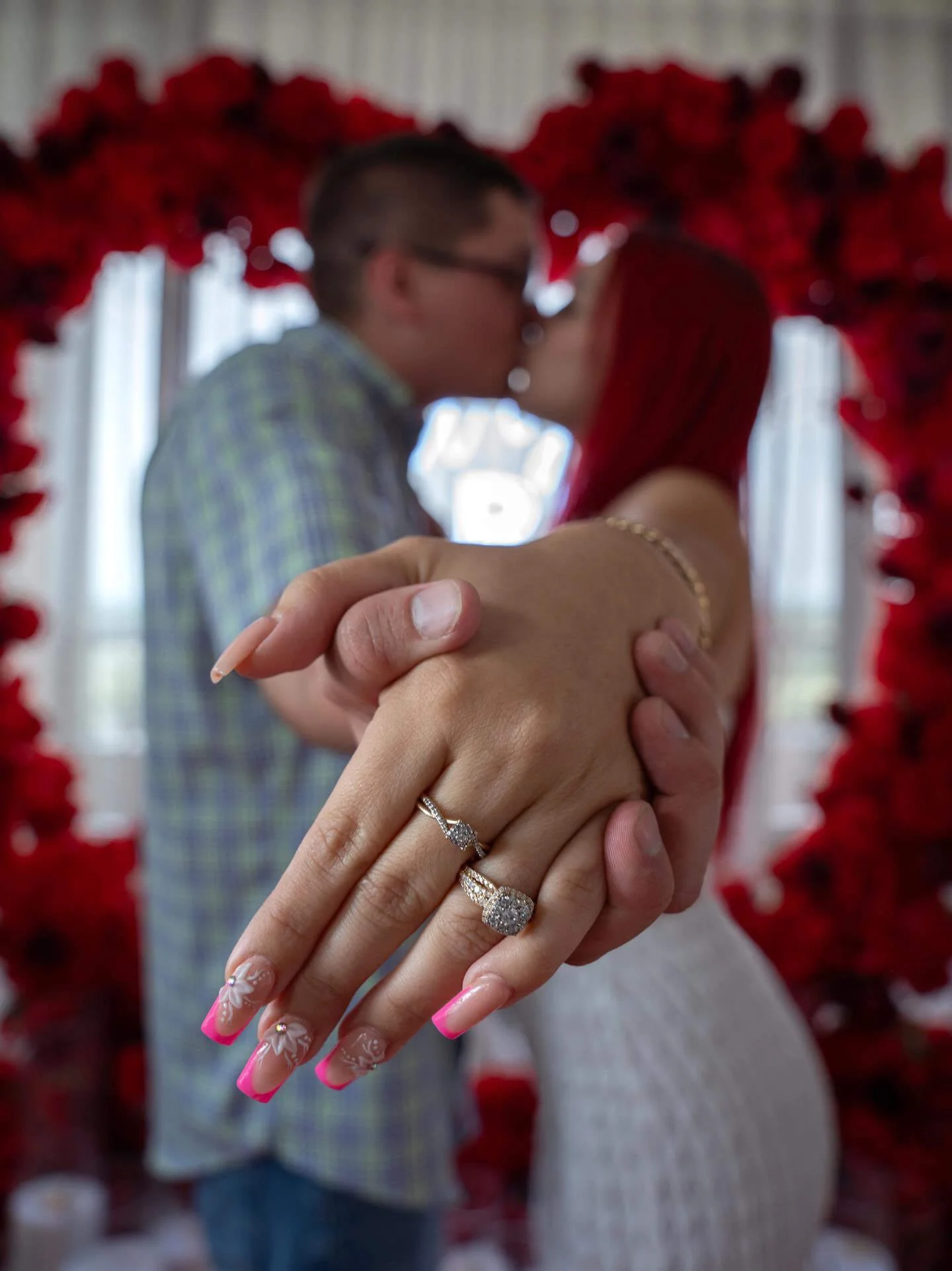 A couple kissing, holding hands, with wedding rings visible, framed by a red heart-shaped decoration.