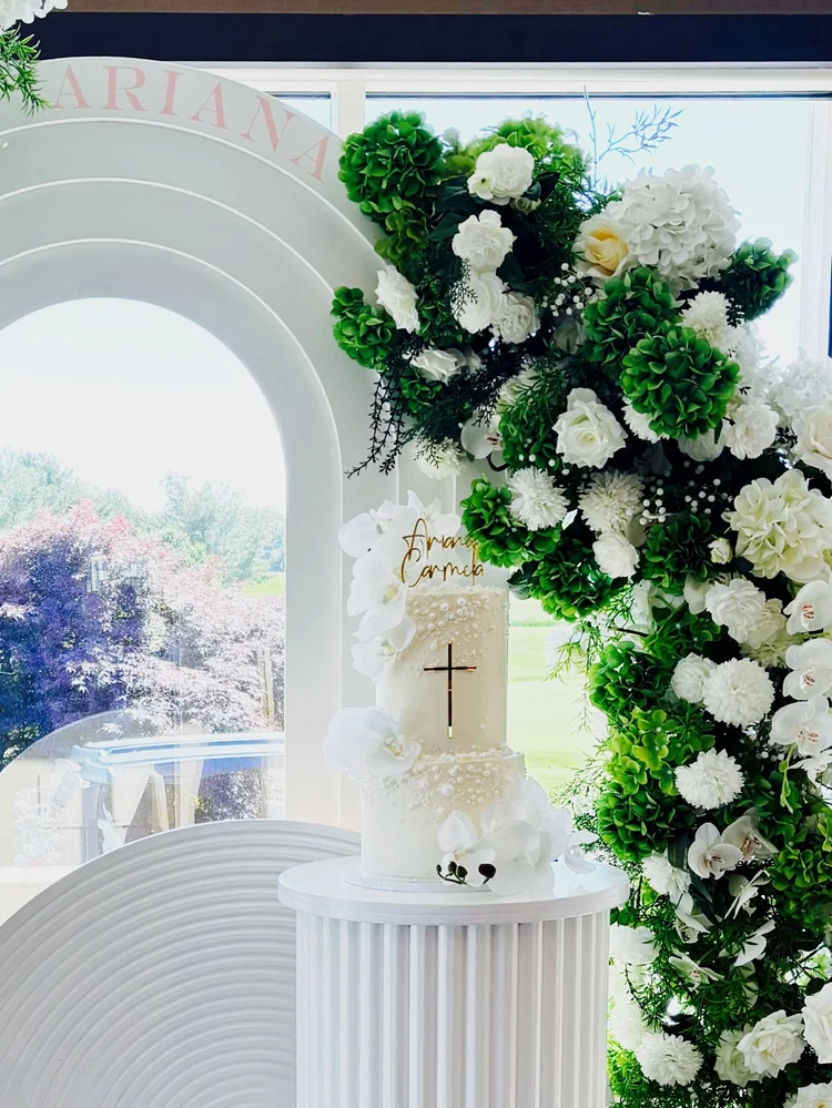 Christening cake display on a white fluted pedestal beside an arch backdrop and a white and green hydrangea floral arch at Chantilly National Golf & Country Club in Centreville, Virginia