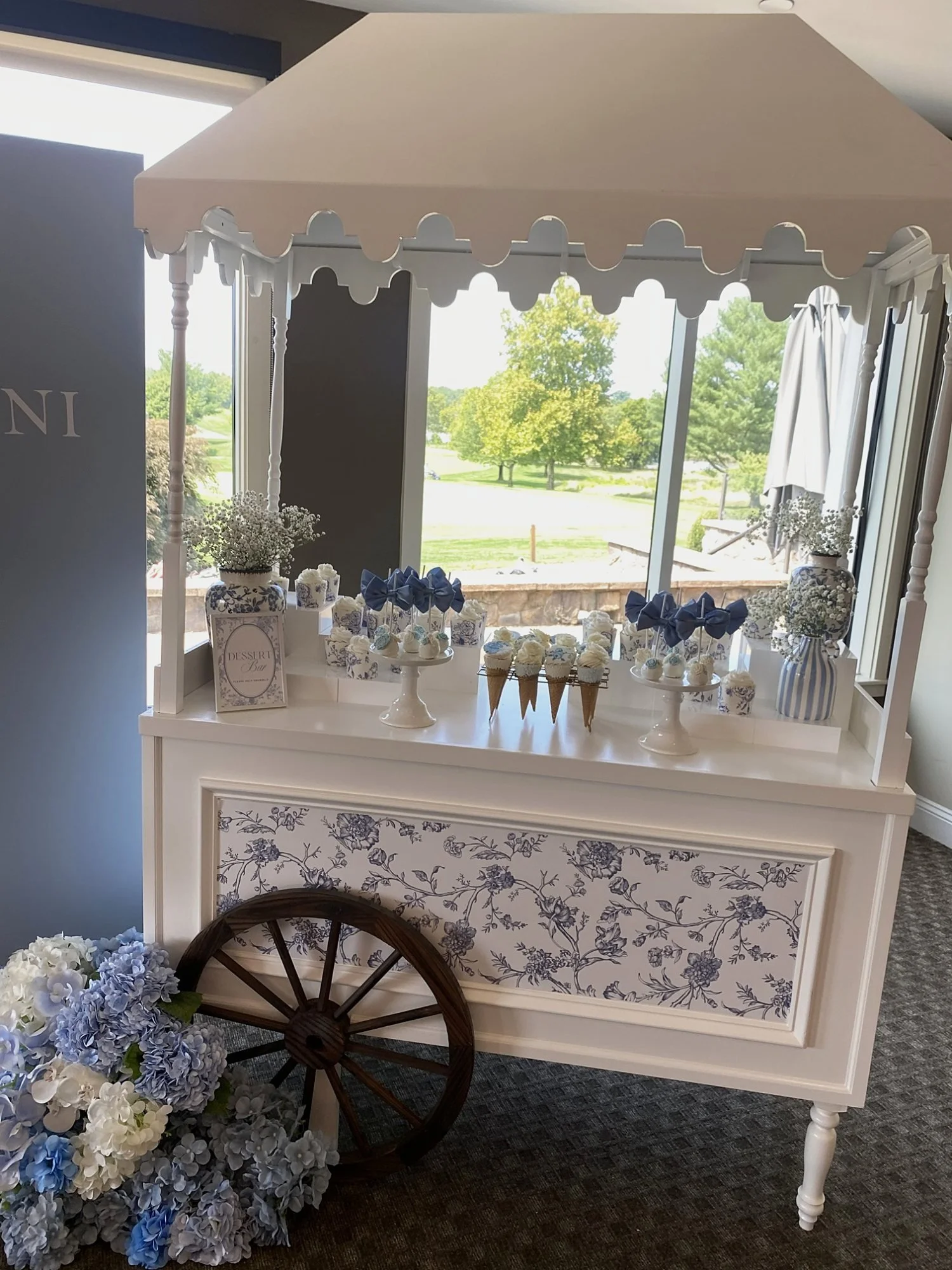 White candy cart rental with a blue toile panel, dessert display and hydrangea floral arrangement at Chantilly National Golf & Country Club in Centreville, Virginia