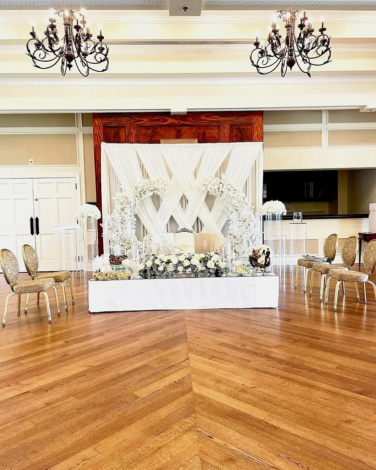Engagement party sweetheart table on a mirrored stage with a white draped crisscross backdrop, white floral arches and clear acrylic pedestals at the Country Club of Fairfax in Virginia