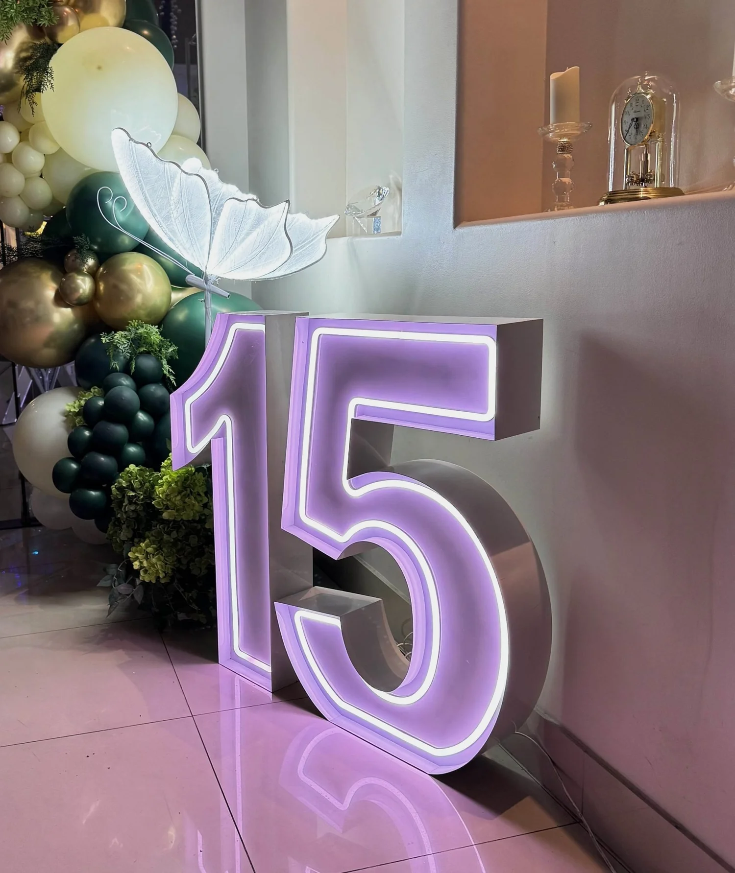 Lit purple neon number 15 beside a glowing LED butterfly and a green, gold and ivory balloon garland