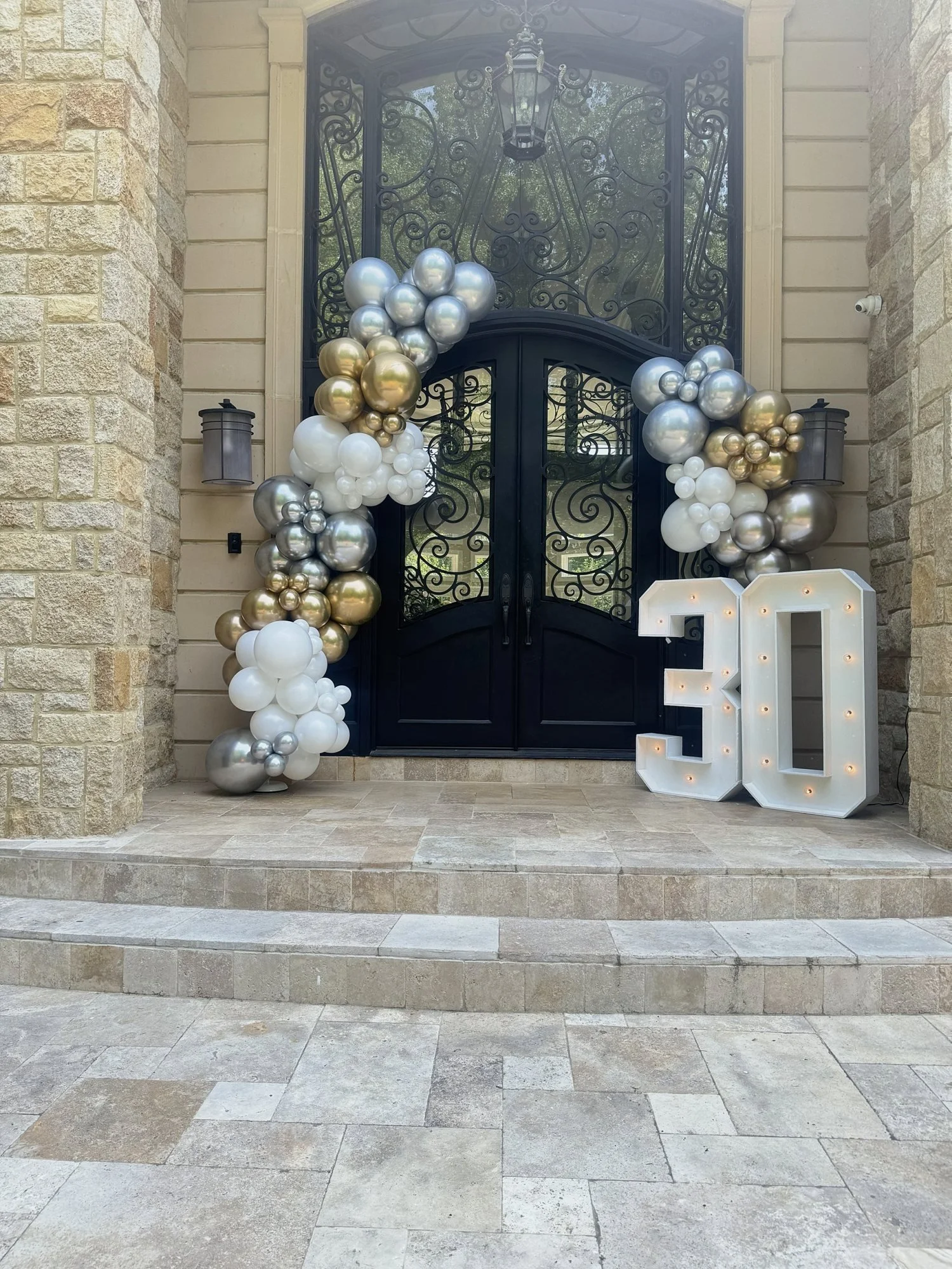 Light-up marquee numbers 30 with a gold, silver and white balloon garland framing a home entrance in McLean, Virginia