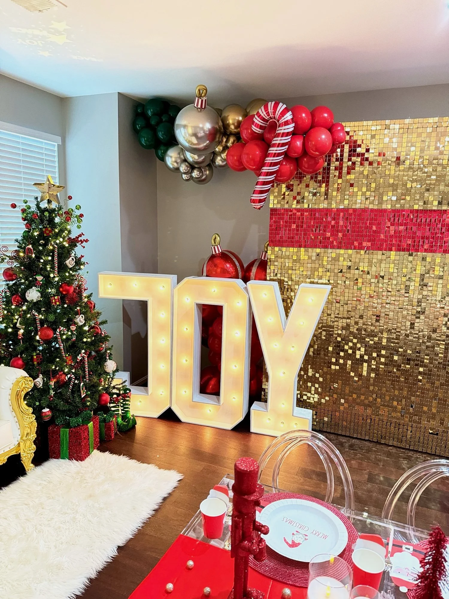 Light-up JOY marquee letters with a sequin backdrop and balloon garland at a Christmas party in Virginia