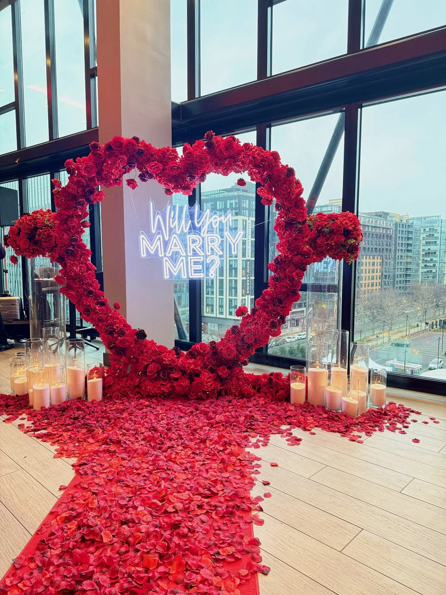 Indoor proposal setup with a red rose heart arch, Will You Marry Me neon sign and rose petals in Washington, DC