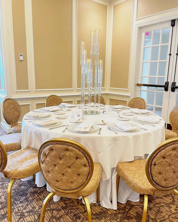Round guest table set with a clear acrylic candelabra centerpiece, white linens and glass charger plates at an engagement party at the Country Club of Fairfax in Virginia
