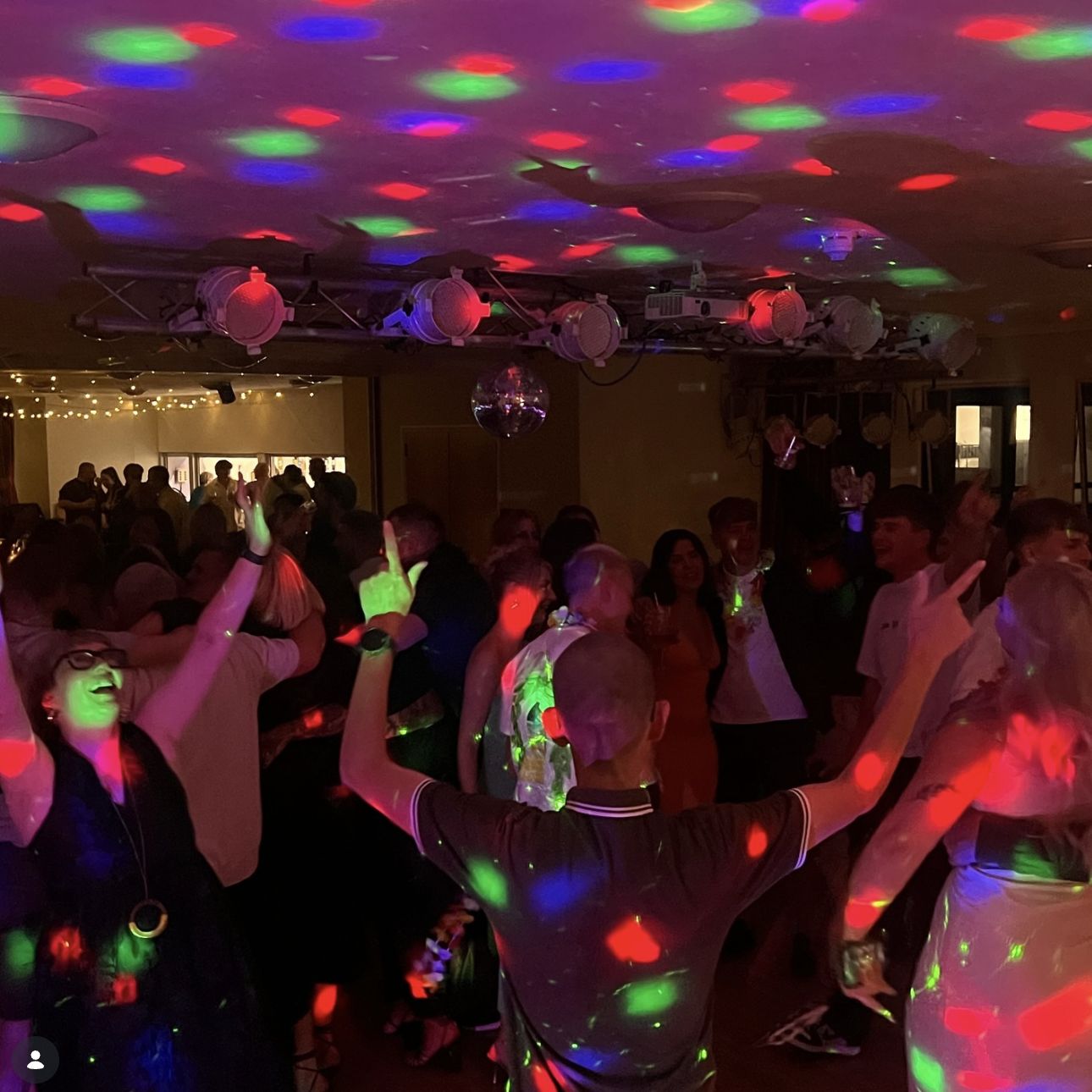 People dancing at a party or celebration under colorful disco lights, with a crowd enjoying the lively atmosphere.