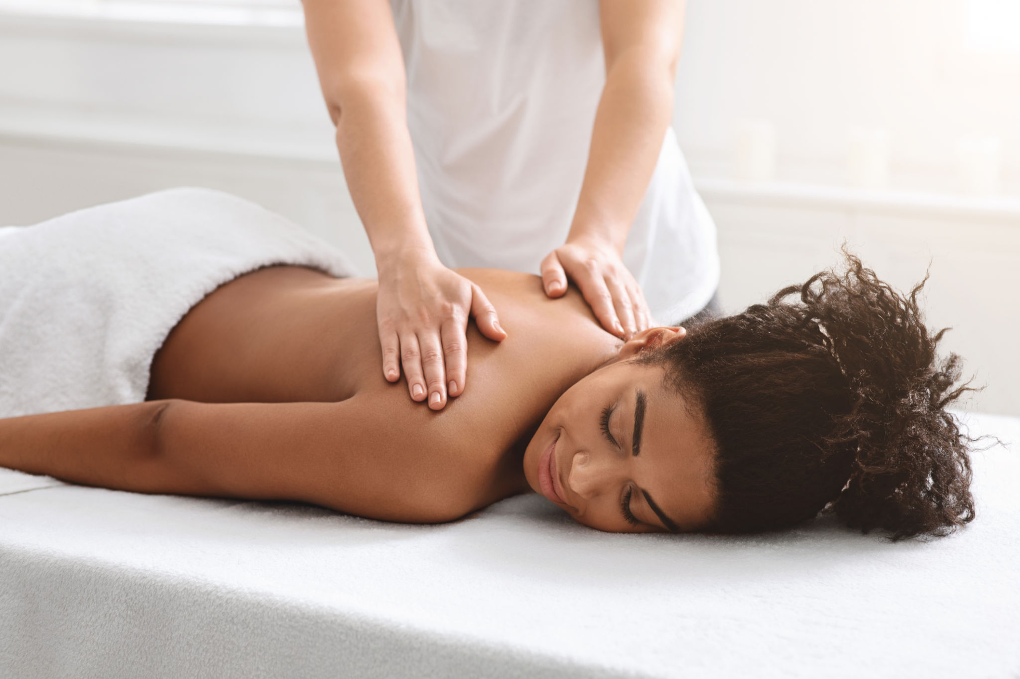 A woman lying face down on a massage table receiving a back massage from a therapist.
