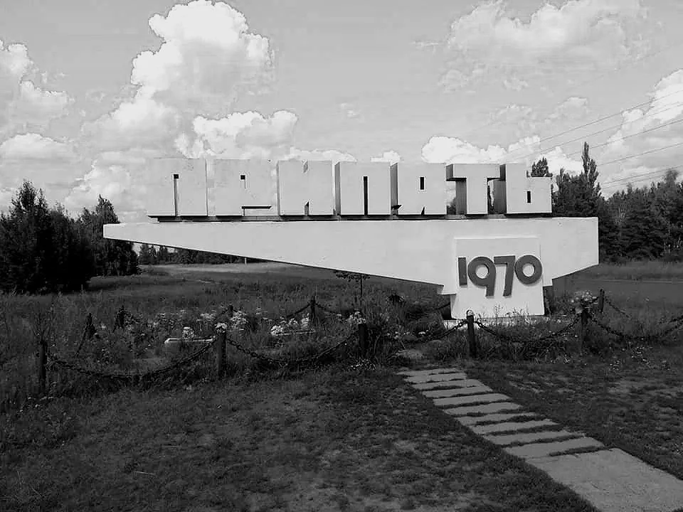 A large sign with the word 'CANTON' and '1970' underneath, situated in a grassy area with a walkway, in black and white.