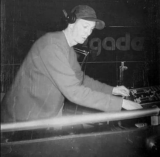 A person wearing headphones and a cap is operating DJ equipment in a dark setting.