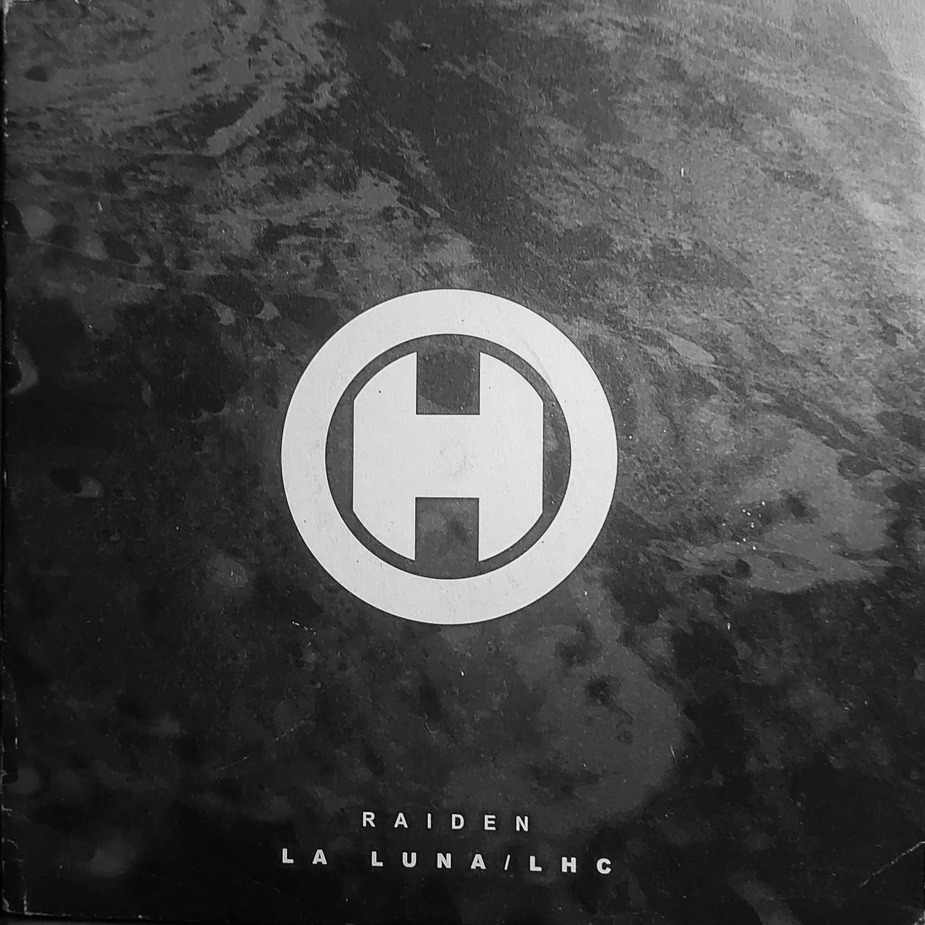 Black and white abstract artwork with a central circular symbol resembling a spaceship or UFO, and the words 'RAIDEN LA LUNA / LHC' at the bottom.